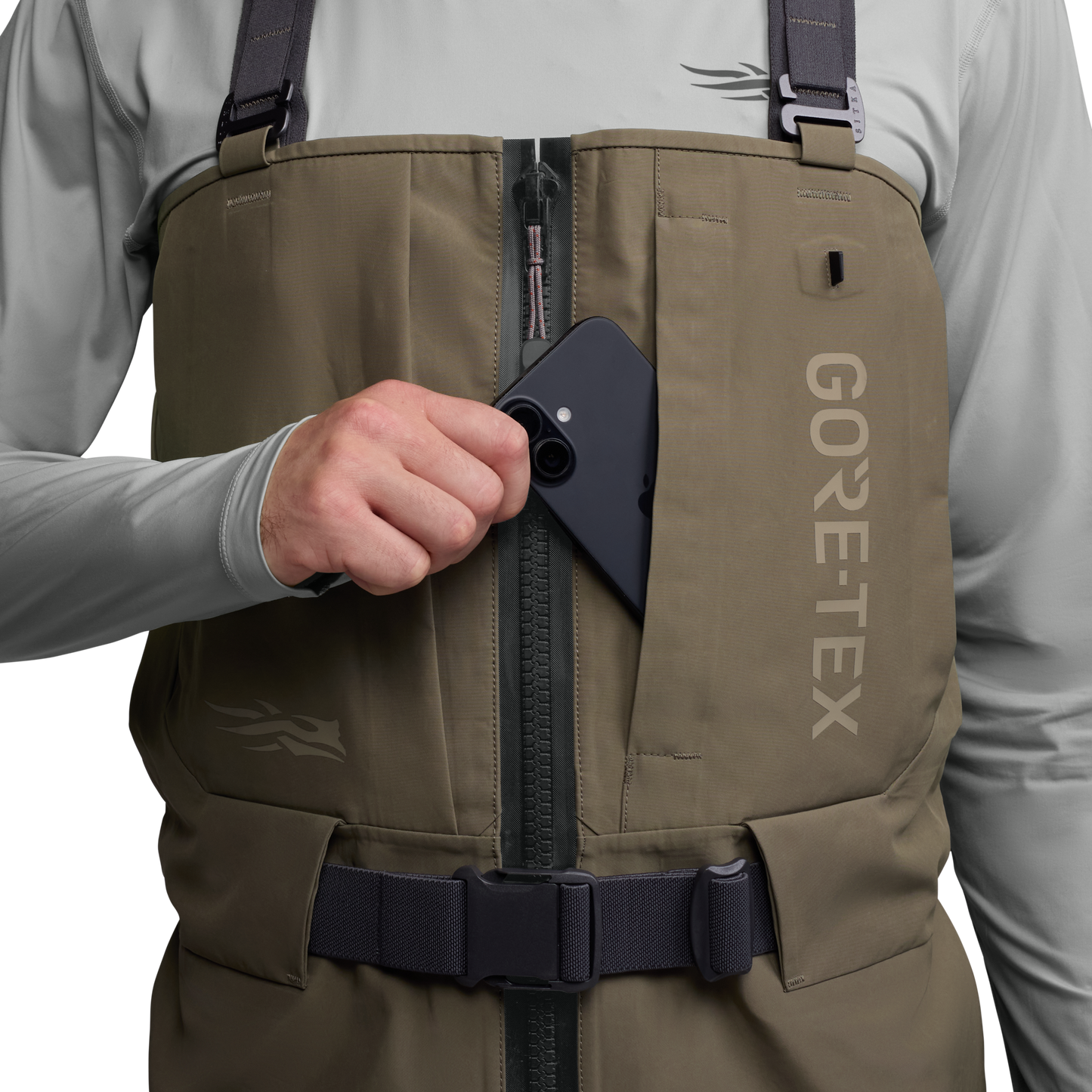 Person wearing a brown GORE-TEX vest with a hand reaching into a pocket.