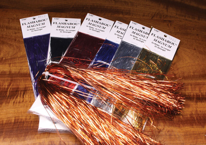 Packs of Hareline Flashabou Magnum in multiple colors including copper, blue, red, silver, and gold, laid out on a wood surface.
