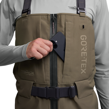 Person wearing a brown GORE-TEX vest with a hand reaching into a pocket.
