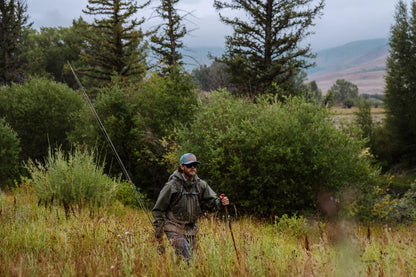 Angler walking through tall grass with a bamboo Fishpond wading staff and fly fishing gear